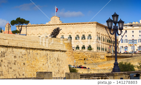 VALLETTA, MALTA - NOVEMBER 12, 2018 - Exterior view of the Auberge de Castille in Castille Square with people walking by VALLETTA, MALTA - NOVEMBER 12, 2018 - Exterior view of the Auberge de Castille in Castille Square with people walking by 141278803