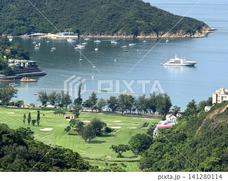 Luxury yacht anchored in a bay with a golf course and lush green hills Luxury yacht anchored in a bay with a golf course and lush green hills 141280114