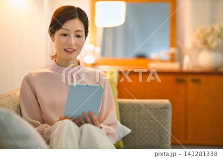 夜部屋でリラックスしてタブレットをを見る40代の女性 夜部屋でリラックスしてタブレットをを見る40代の女性 141281338