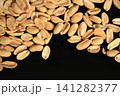 roasted peanuts scattered across a black surface, highlighting their crunchy texture and rich golden-brown color with dramatic contrast for snack packaging, food advertising, restaurant menus 141282377