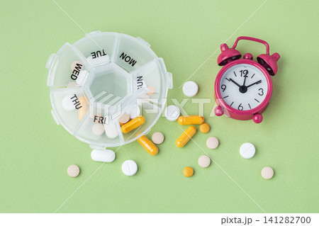 Pill box organizer with medication and alarm clock on green background Pill box organizer with medication and alarm clock on green background 141282700