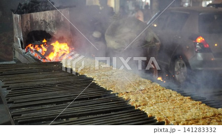 Meat kebabs grilling over hot coals on a large grill, smoke rising, street food Meat kebabs grilling over hot coals on a large grill, smoke rising, street food 141283332