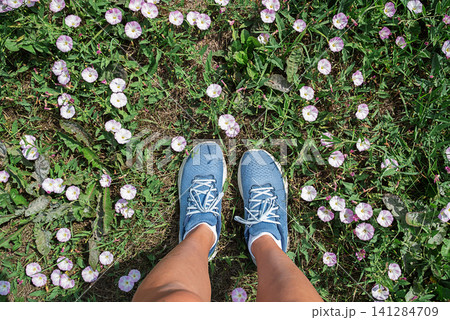 Woman wearing blue sneakers standing on field with small white and pink flowers. Woman wearing blue sneakers standing on field with small white and pink flowers. 141284709