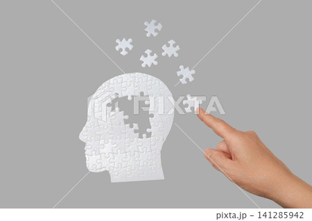 A hand positions a puzzle piece into a human head silhouette design A hand positions a puzzle piece into a human head silhouette design 141285942