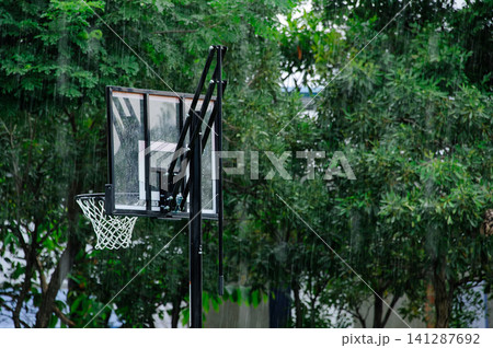 raining in the outdoor basketball field with a basketball hoop with many trees in background raining in the outdoor basketball field with a basketball hoop with many trees in background 141287692