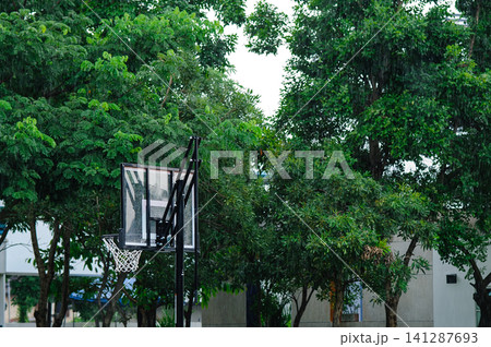 raining in the outdoor basketball field with a basketball hoop with many trees in background raining in the outdoor basketball field with a basketball hoop with many trees in background 141287693