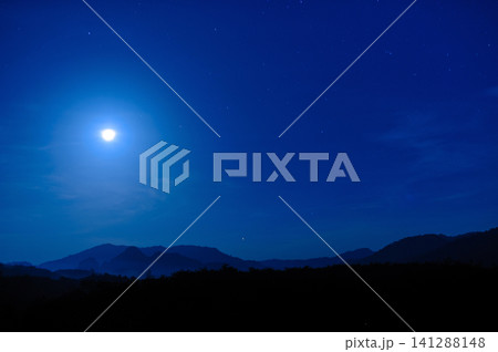 moonlight in the blue clear sky with a silhouette foreground of a forest and hill 141288148