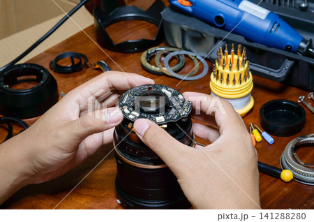 two hands of a man doing work with broken camera lens to fixing it at working table two hands of a man doing work with broken camera lens to fixing it at working table 141288280