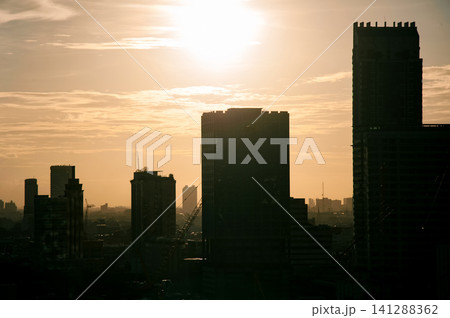 beautiful warm toned color of sky  and the sun on a top of silhouette buildings  in  a city photo with some noise and gain 141288362
