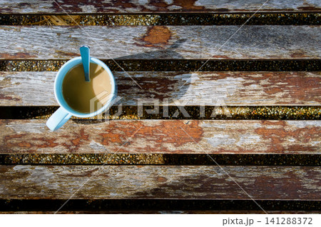 a cup of coffee on wooden bench in shade of morning sunrise with tea spoon looked like 7 o'clock's wall clock a cup of coffee on wooden bench in shade of morning sunrise with tea spoon looked like 7 o'clock's wall clock 141288372