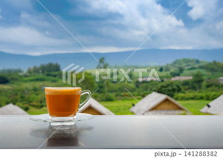 hot Thai's style milk tea in a cup with mountain view when a raining is coming from somewhere faraway 141288382