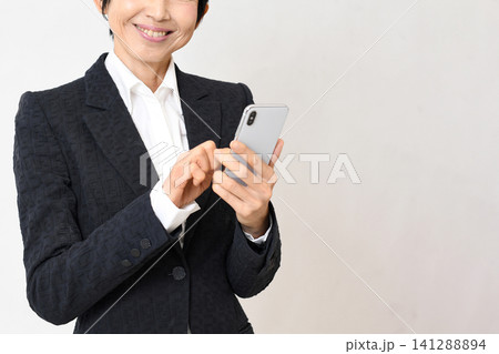 笑顔でスマホを持つスーツ姿のアジア人女性 笑顔でスマホを持つスーツ姿のアジア人女性 141288894