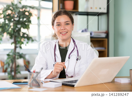 Young woman in white coat working with laptop in medical office Young woman in white coat working with laptop in medical office 141289247