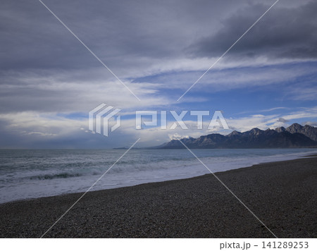 beautiful beach and serene ocean with a dramatic mountain range backdrop beautiful beach and serene ocean with a dramatic mountain range backdrop 141289253