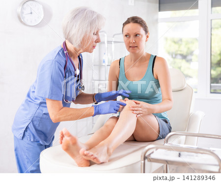Elderly woman doctor examining leg of female patient Elderly woman doctor examining leg of female patient 141289346