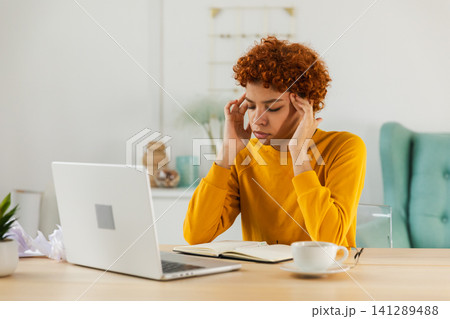 African woman touching temples experiencing stress. Girl at home office tired of working feeling headache sick rubbing temples forehead. Long laptop usage computer vision syndrome. Office syndrome African woman touching temples experiencing stress. Girl at home office tired of working feeling headache sick rubbing temples forehead. Long laptop usage computer vision syndrome. Office syndrome 141289488