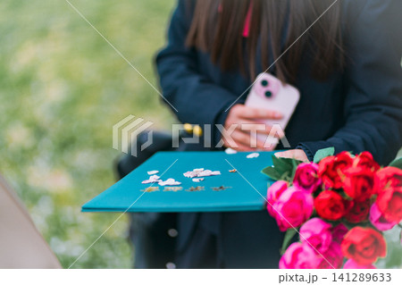 卒業証書と薔薇の花束を持ちスマホ撮影する制服女子高生 卒業証書と薔薇の花束を持ちスマホ撮影する制服女子高生 141289633