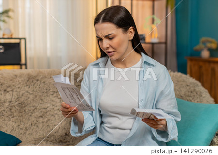 Young woman disappointed stressed sits on sofa holding bills worried financial problems asking why Young woman disappointed stressed sits on sofa holding bills worried financial problems asking why 141290026