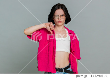 Woman shows thumbs down with serious expression expressing dislike disagreement or disappointment 141290129