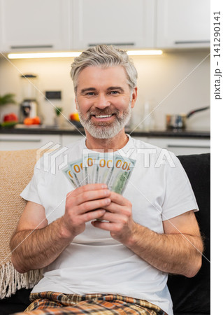 Middle-aged man counts money cash dollars smiles at plans purchase salary bonus savings investment Middle-aged man counts money cash dollars smiles at plans purchase salary bonus savings investment 141290141
