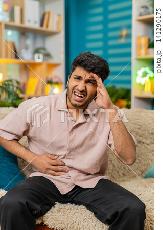 Indian man on home sofa feels side pain with stressed face stomach ache health problem indoors issue 141290175