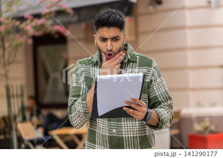 Indian man finding document error walking in city street feeling shocked and disappointed outdoors 141290177