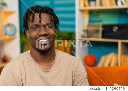 African American young man on home sofa sitting relaxed looking at camera with soft smile indoors African American young man on home sofa sitting relaxed looking at camera with soft smile indoors 141290336