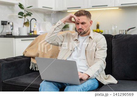 Young man sees defeat on laptop touches forehead sighs and clicks retry after bad news on screen sad Young man sees defeat on laptop touches forehead sighs and clicks retry after bad news on screen sad 141290569