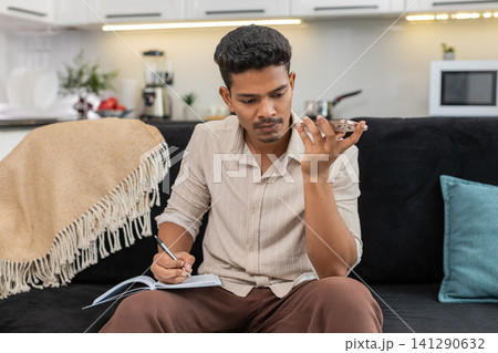 Indian man on speakerphone makes business call writes clear notes in notebook focused conversation 141290632