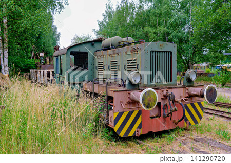 Abandoned vintage narrow gauge train locomotive standing in high green grass next to forest Abandoned vintage narrow gauge train locomotive standing in high green grass next to forest 141290720