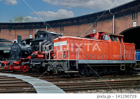 Row of vintage steam and diesel locomotives parked outside an old brick roundhouse Row of vintage steam and diesel locomotives parked outside an old brick roundhouse 141290729