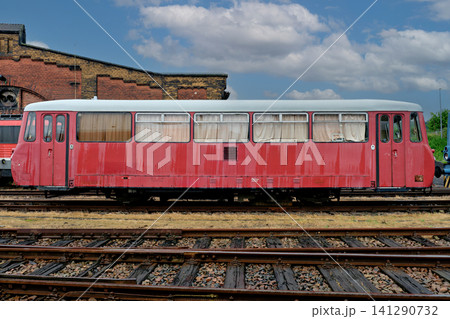 Side view of a retro red railbus carriage on tracks next to an old brick depot building Side view of a retro red railbus carriage on tracks next to an old brick depot building 141290732