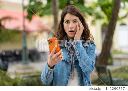 Young woman shocked by bad news on smartphone walking in city street feeling sad during urban trip Young woman shocked by bad news on smartphone walking in city street feeling sad during urban trip 141290757