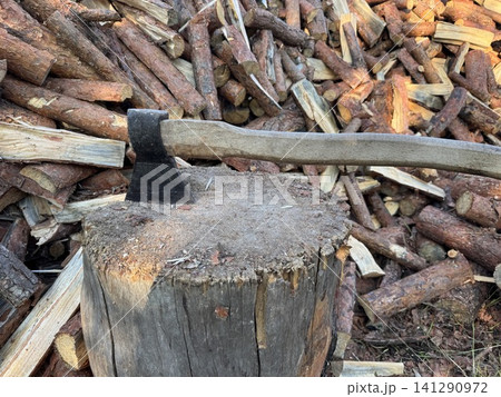 Axe in Chopping Block with Stacked Firewood Background Axe in Chopping Block with Stacked Firewood Background 141290972