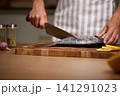 Chef hands preparing raw fish with a knife for cooking, cleaning and scaling fresh seafood on a wooden cutting board in a kitchen 141291023