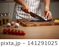 Professional chef's hands cutting raw fish on a wooden board, preparing a fresh seafood meal with vegetables 141291025
