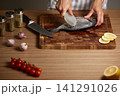 Chef scaling fresh fish on a wooden cutting board, preparing ingredients for a healthy seafood meal with spices and lemon slices 141291026