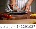 Female hands preparing fresh sea bream on a wooden cutting board, removing scales for cooking healthy seafood 141291027