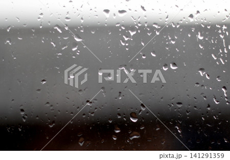 Close up of raindrops and water droplets on window glass. Abstract wet window pane background with blurred dark grey backdrop on a rainy day Close up of raindrops and water droplets on window glass. Abstract wet window pane background with blurred dark grey backdrop on a rainy day 141291359
