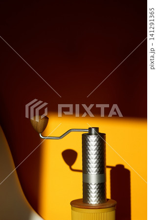 Manual coffee grinder with hard shadow on bright yellow and brown background. Minimalist composition with manual silver burr coffee mill and geometric shadows, specialty coffee brewing concept Manual coffee grinder with hard shadow on bright yellow and brown background. Minimalist composition with manual silver burr coffee mill and geometric shadows, specialty coffee brewing concept 141291365