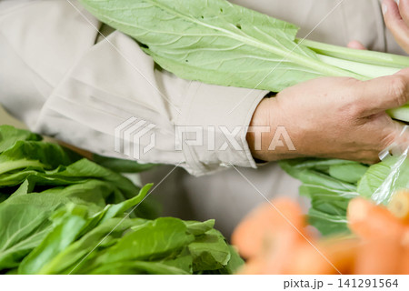 Fresh vegetables for sale at a local market stall, featuring carrots in a white plastic crate and leafy greens in the background 141291564