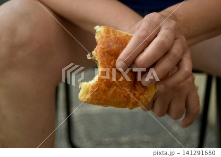 Closeup of a hand holding a bitten chocolate pastry with a soft blurred background. Fresh baked breakfast pastry enjoyed as a snack or morning treat. 141291680