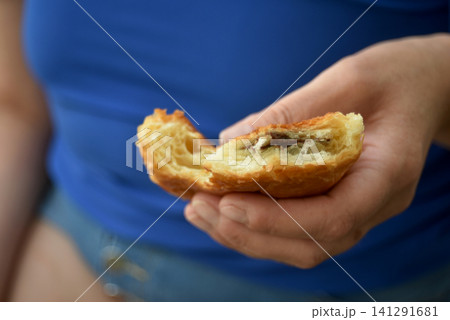 Closeup of a hand holding a bitten chocolate pastry with a soft blurred background. Fresh baked breakfast pastry enjoyed as a snack or morning treat. 141291681