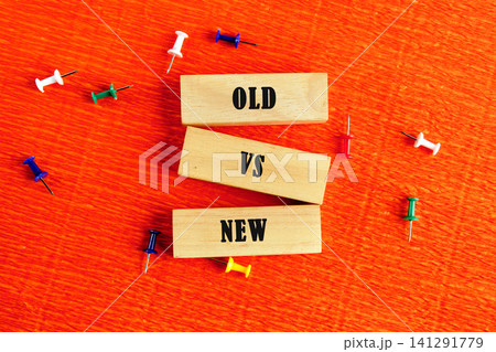 Wooden blocks display the words old and new with a vs in between. Colorful push pins are scattered on an orange surface, creating a vivid scene of contrast 141291779