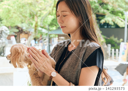 神社で愛犬を抱いて手を合わせて祈る若い女性 141293573