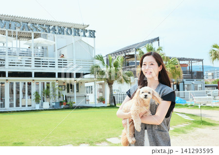 海辺のおしゃれなカフェの前で愛犬を抱く笑顔の若い女性 141293595