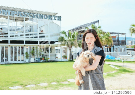 海辺のカフェの芝生広場で愛犬を抱く笑顔の若い女性 海辺のカフェの芝生広場で愛犬を抱く笑顔の若い女性 141293596