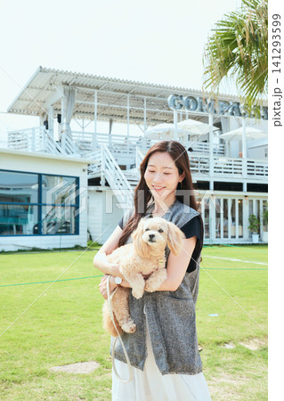 愛犬を抱いて笑顔の若い女性と緑の芝生が広がるドッグフレンドリーカフェ 愛犬を抱いて笑顔の若い女性と緑の芝生が広がるドッグフレンドリーカフェ 141293599