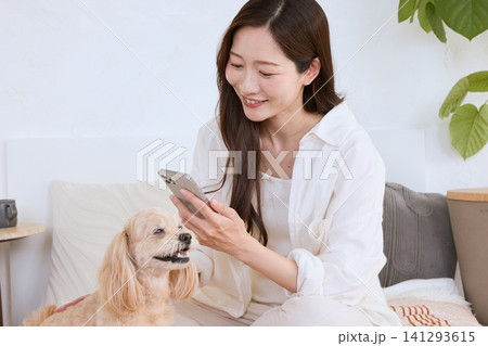 リビングでスマートフォンを見ながら愛犬と過ごす笑顔の若い女性 141293615