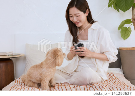 ベッドの上で愛犬と寛ぐマグカップを持った笑顔の若い女性 ベッドの上で愛犬と寛ぐマグカップを持った笑顔の若い女性 141293627